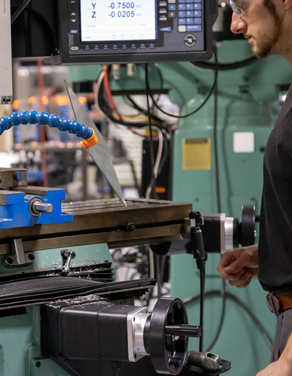 Student in front of machine holding a sheet of metal