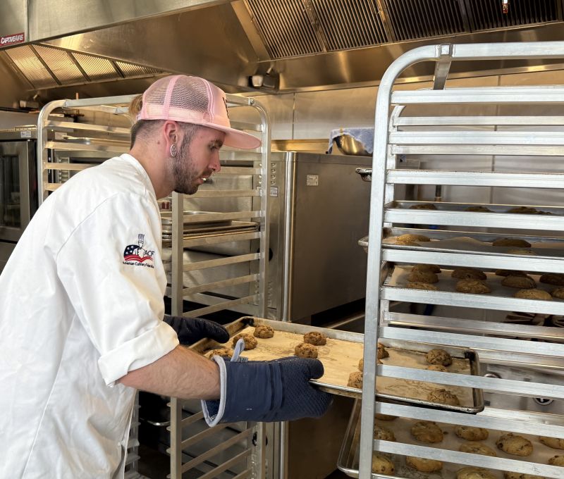 A culinary student puts a tray of cookies onto a rolling cart during class at Lakeshore College.